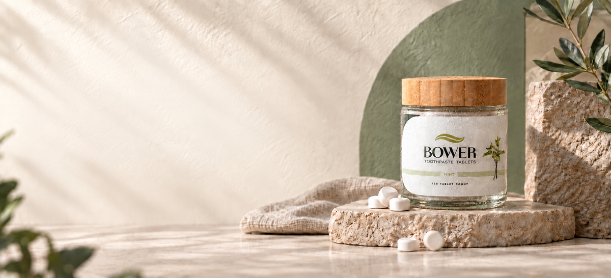BOWER mint toothpaste tablets in a glass jar on a stone stand, framed by soft greenery and warm cream walls